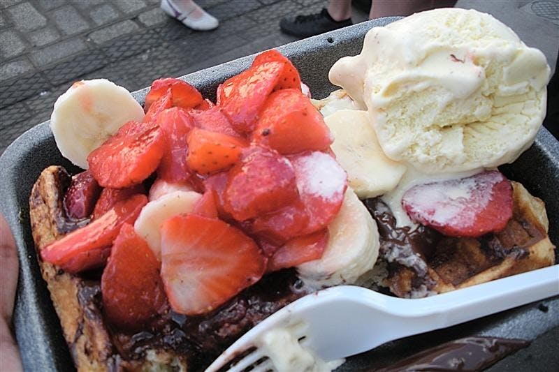 A Belgian waffle drizzled with chocolate syrup and topped with strawberries and ice cream from the Camden Lock Market in London.  