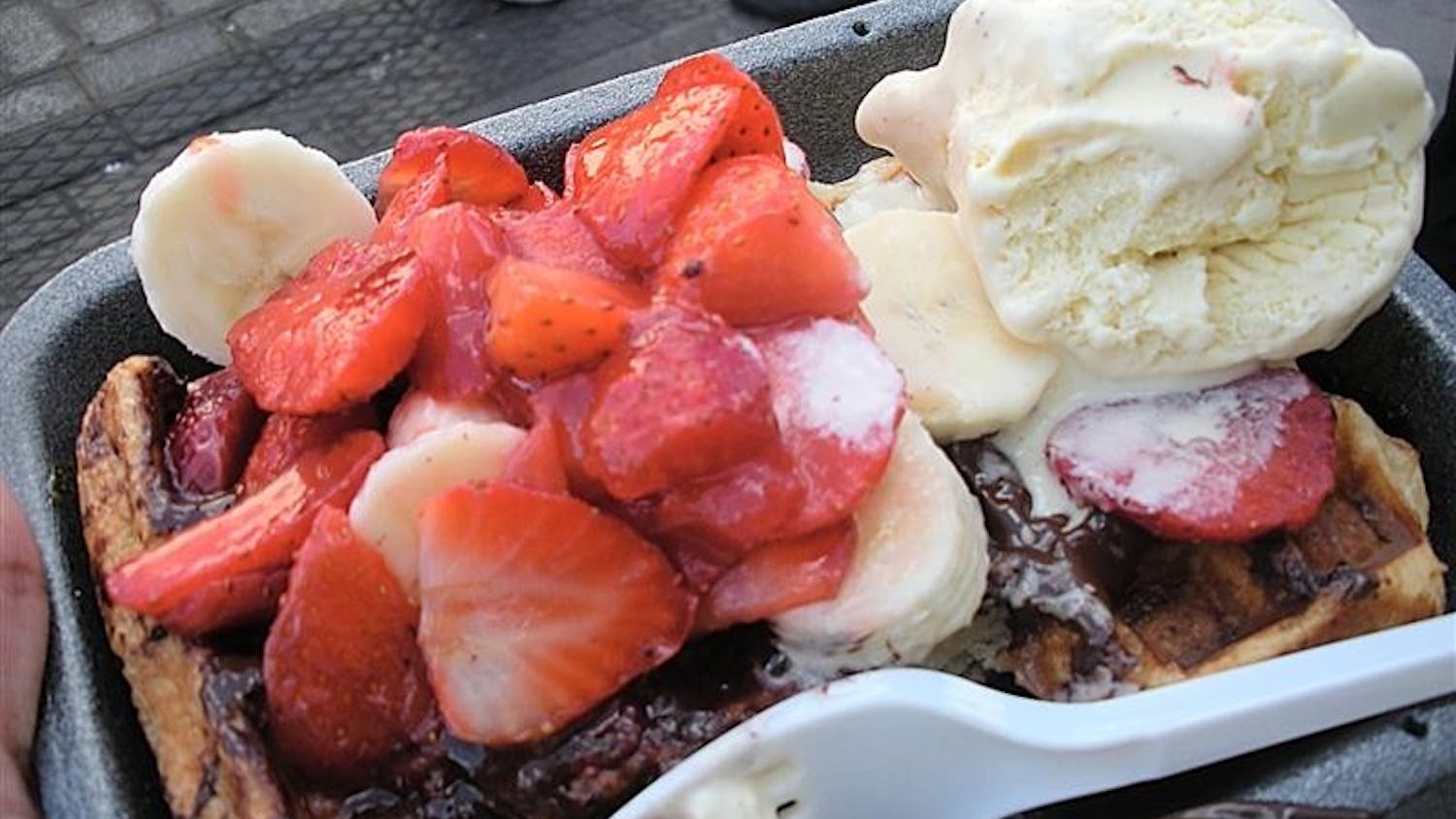 A Belgian waffle drizzled with chocolate syrup and topped with strawberries and ice cream from the Camden Lock Market in London.  
