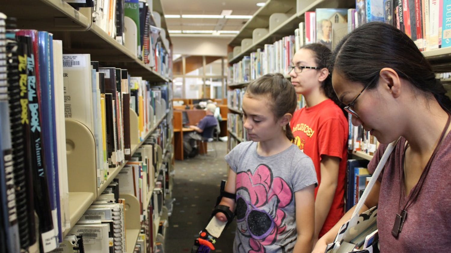 Violet Hall looks at music books with her mother, Milet Hall, and older sister at the Monroe County Public Library. Violet just started playing the violin with the help of her 3D printed arm, which was designed by an IU lecturer. 