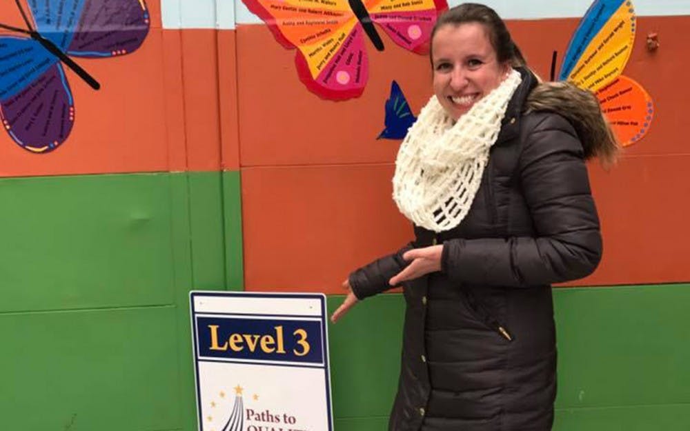 Childcare Coordinator Marcella Ettinger displays the level 3 achievement outside the daycare, in the courtyard at Middle Way House.