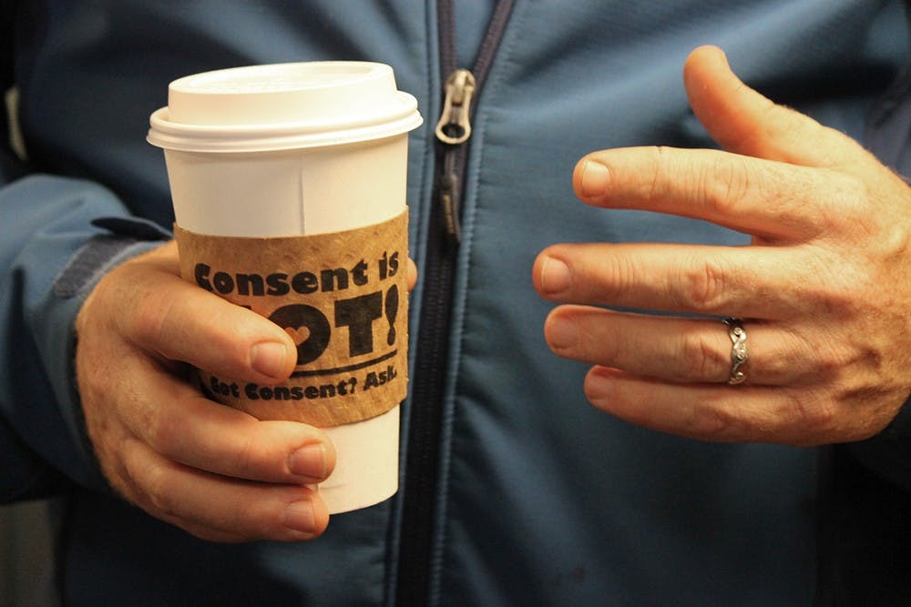 Patrick Hanaway holds his latte from Soma Coffeehouse with the "Consent is Hot!" cardboard sleeve on the outside. The sleeves are part of Sexual Assault Awareness Month.