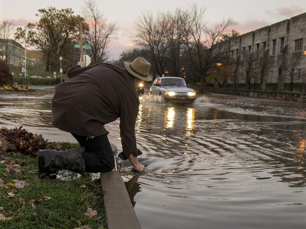 Mike Webb, a maintenance worker at the Indiana Memorial Union, removes leaves and debris from storm drains in an attempt to lower the water level at the intersection of 7th and Woodlawn as traffic continue to risk driving through the high water. The intersection flooded following heavy rains that accompanied severe storms Sunday. “I don’t know who’s supposed to do this but I just grabbed the first boots I could find and came out here,” Webb said.