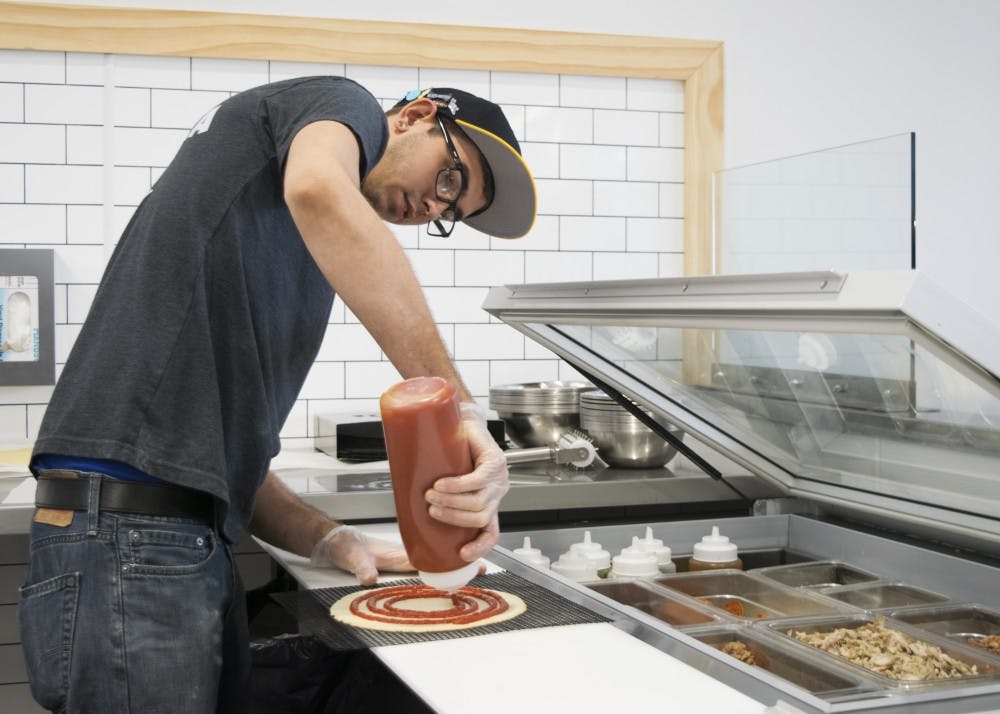 Grimsley squeezes sauce onto a pizza for a customer. Azzip's pizzas are made to order in front of customers, who can choose from a wide array of ingredients to customize their pizza.
