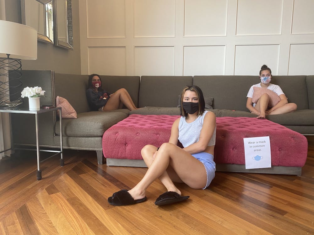 <p>IU sophomores (from left to right) Maxine Gordon, Ravyn Sweat and Noa Gauthier sit in the quarantined Gamma Phi Beta sorority living room. &quot;Wear a mask in common areas,&quot; a sign reads.</p>