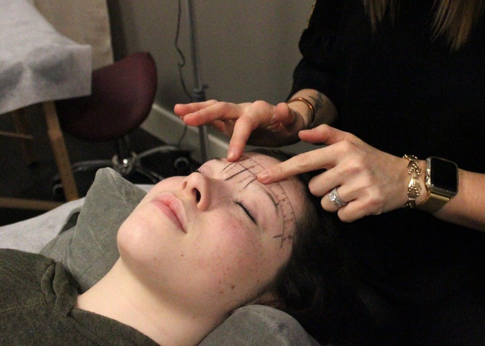 Shaena Litwin, the owner of a microblading studio off North Walnut Street, measures and plans her client's eyebrows on Tuesday. Eyebrows should be sisters, not twins in terms of style, she said. 