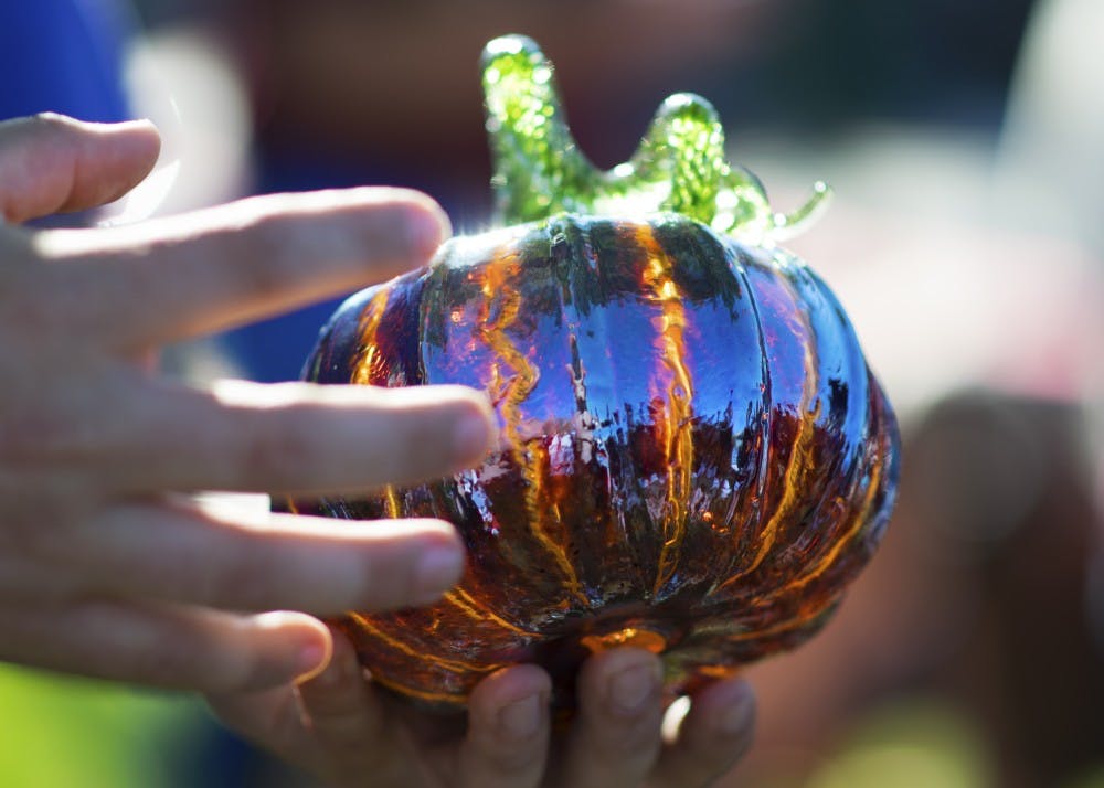 Tomas Gregg, a volunteer who has worked with the Bloomington Creative Glass Center for seven years, demonstrates how a crackle effect is achieved on some of the pumpkins at the Great Glass Pumpkin Patch on Saturday morning on the Monroe County Courthouse lawn. The crackle effect uses two layers of glass to create the two-tone effect.