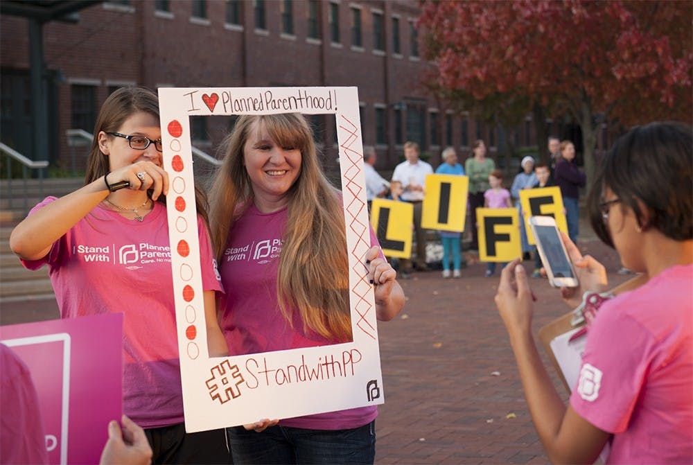 Planned Parenthood supporters take a photo in show of their support against the backdrop of pro life supporters outside the Bloomington City Council office before the council meeting on Wednesday. The city council heard a resolution in support of the local planned parenthood clinic during the meeting.