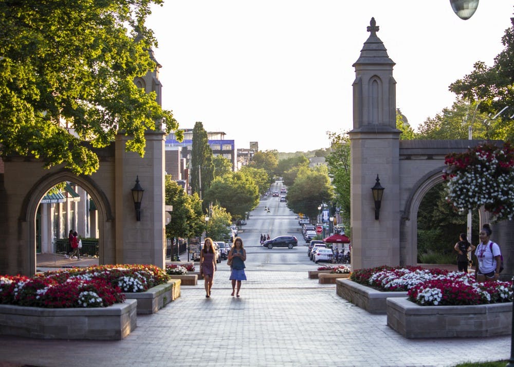 <p>People walk through the Sample Gates on June 27 near Franklin Hall. The Sample Gates are considered a gateway to IU’s campus.&nbsp;</p>