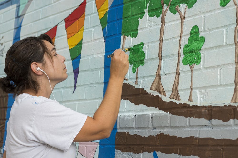 <p>Eva Rholfing Allen paints a section of the mural in 2017 in Peoples Park. A release from the Bloomington Arts Commission encourages artists to <a href="https://bloomington.in.gov/sites/default/files/2020-06/Trades%20Garage%20District_RFQ_FINAL.pdf" target="">submit proposals</a> for new artwork which will be located near downtown Bloomington at the Trades District Garage.</p>
