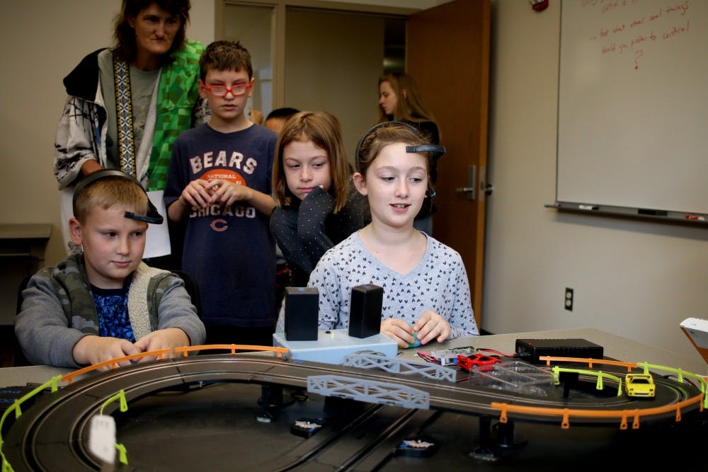 孩子们戴着可以追踪脑电波的耳机，脑电波驱动着玩具车在轨道上行驶。该游戏是印第安纳大学科学节的一部分，该节欢迎人们来学习科学的不同方面。