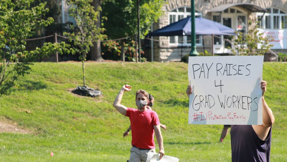 2020年8月24日，在Dunn Meadow，一名抗议者手持“4名毕业生工人加薪”的标语，抗议工资不足。每年，8%的毕业生工人'；向IU支付回报。