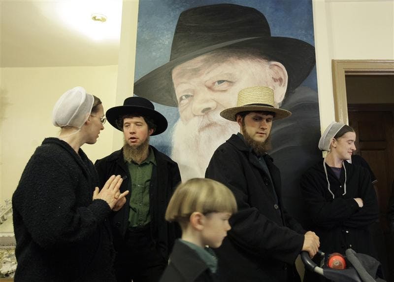 Anna Stoltzfus, left, talks with her husband Matthew Stolzfus in front of a portrait of the late Lubavitcher Rabbi Menachem Schneerson, while taking a tour with John Lapp, center, his son Jonathon, 6, and wife Priscilla, at a museum Tuesday in the Crown Heights neighborhood of Brooklyn, New York. The city's ultra-Orthodox Jews took a group of Pennsylvania Amish on a walking tour of their world Tuesday, saying their communities are naturally drawn to each other with a commitment to simpler lifestyles. 