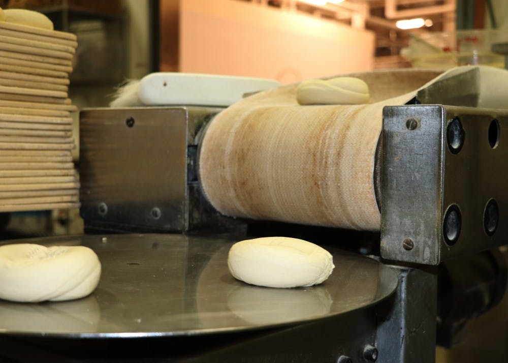 <p>On the other end of the machine, bagels come out and land on a spinning disc before being placed on racks. Tritan said they use 500 pounds of flour a day on average.</p>