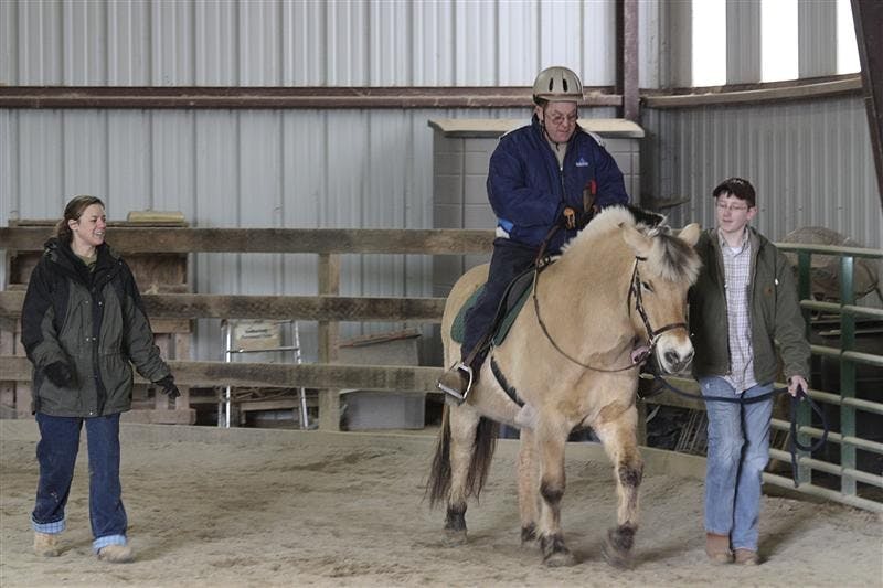 Trainer Jennifer Lung watches as Steve McGovern and his horse are guided by Ben Slinkard Tuesday afternoon at the PALS arena. McGovern is 43 years old and has been riding at People and Animal Learning Services for five years.