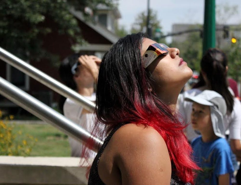 A student wearing eclipse glasses staring up at the sun.