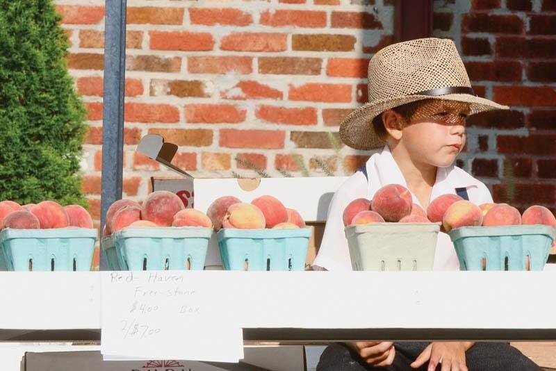 LOCAL FLAVOR - Jacob Grabar of Odon, Ind., enjoys an ice cream sandwich as things wind down at the Tuesday Market in the Bloomingfoods Near West parking lot. Jacob helps his father Daniel operate the stand from which they have been selling locally grown fruit and vegetables for nine years.