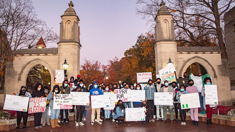 Attendees of the #AfricaisBleeding Candlelight Vigil hold up signs Friday at the Sample Gates.