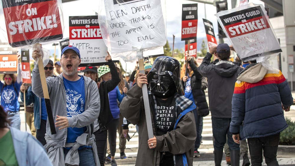 Writers Joe Henderson (left) and Montserrat Luna, wearing a Darth Vader helmet (right) strike with other members of the Writers Guild of Americaon May 4, 2023, in Universal City, California. After an unsuccessful six weeks of negotiations with the Alliance of Motion Picture and Television Producers, members of the Writers Guild decided to go on strike outside of NBC/Universal Studios.