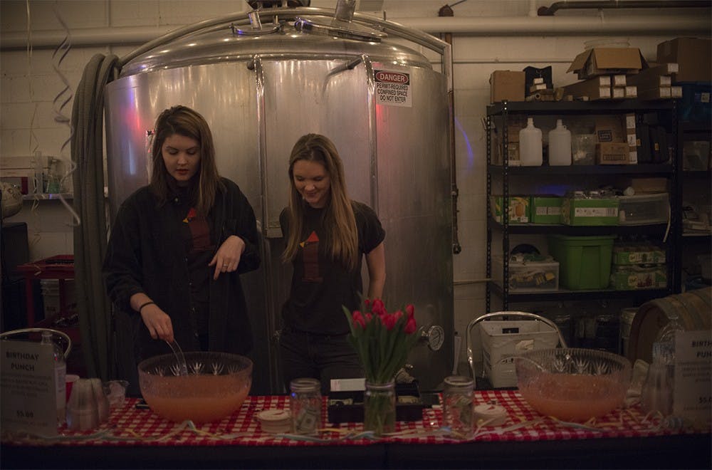 Hannah Boone (left) and Emma Sullivan wait to serve a drink called Birthday Punch during the one year anniversary of Cardinal Spirits on Saturday. Cardinal Spirits tries to source Indiana products in their process, including the machines to make the liquor.