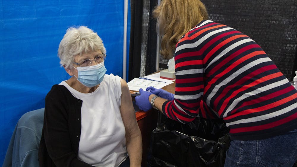 IU Health Nurse Anne Fuson在24日在Monroe会议中心给IVA Gloss提供了第二剂Modica Covid-19疫苗。在星期五的会议期间，布卢明顿市宣布，出于在印第安纳州有资格收到Covid-19疫苗的国家学生。