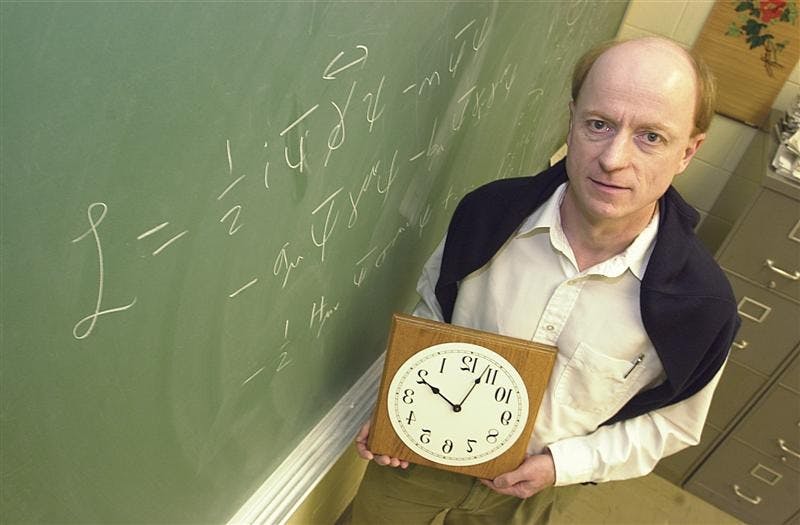 Theoretical physicist Alan Kostelecky poses in his office next to a portion of the equation used to design his backwards clock.