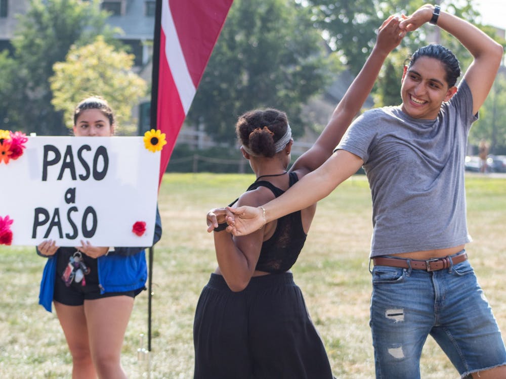 IU sophomore Sharina Hernandez watches IU sophomores Trinity Barnes and Israel Robles dance near the Paso a Paso Involvement Fair booth Aug. 26, 2021, in Dunn Meadow. Paso a Paso is a cultural outreach dance team at Indiana University, according to the group&#x27;s beINvolved page.