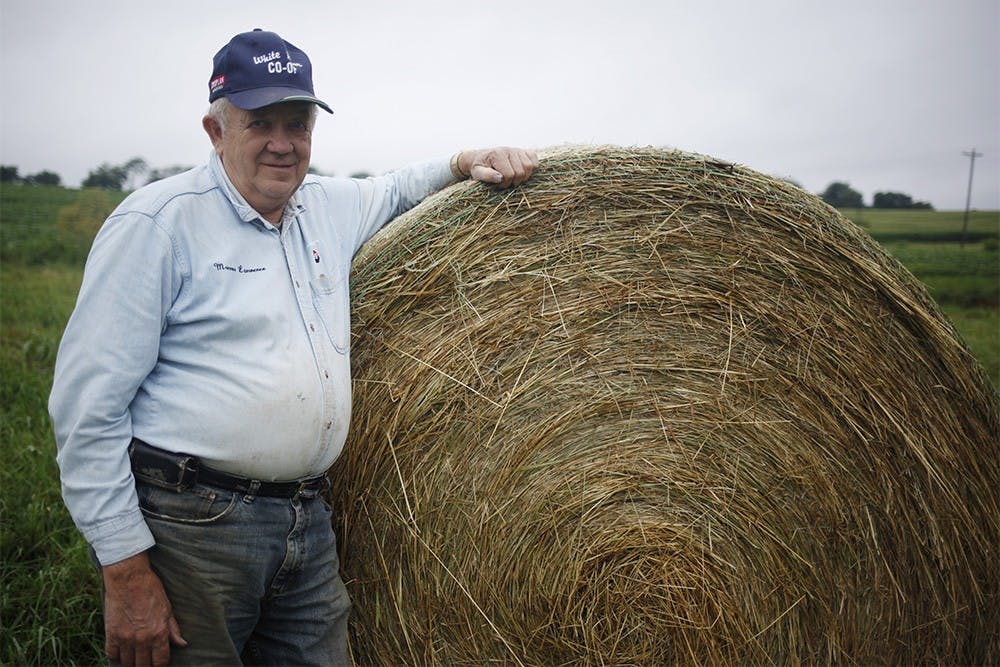 Joe Peden poses in front of a bale of hay on his property at Peden Farm in Bloomington on Wednesday.  While the rain has not affected his crops directly, the farm has not been able to harvest hay due to it not being dry.  Peden usually expects to harvest all of his hay by the end of June, he says, but so far he has only harvested 25 out of 800 bales.