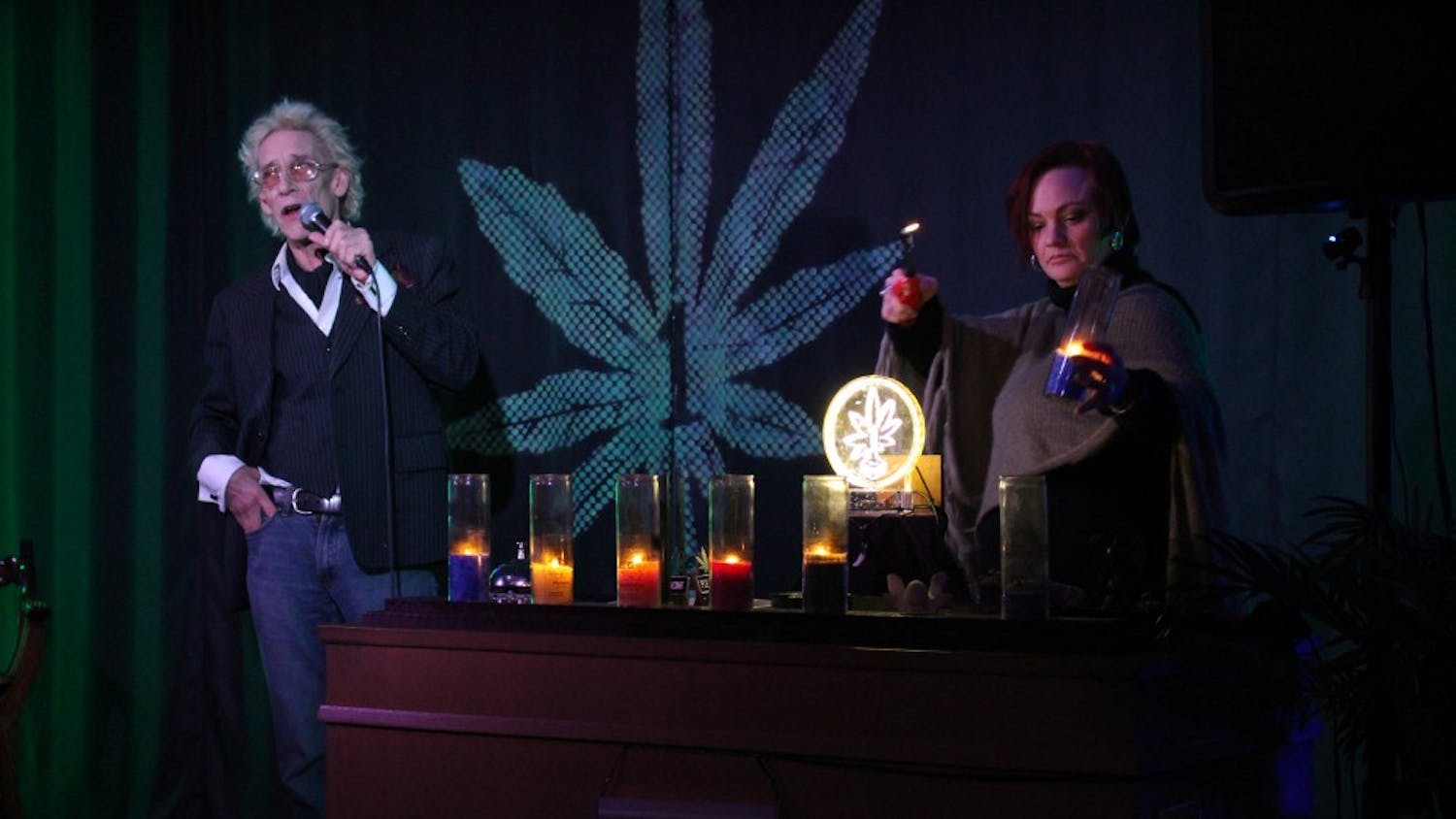 Bill Levin talks about how the candles represent the seven focus areas as a member of the First Church of Cannabis, Roo Gelarden, lights the candles. The candles represent the following: live, love, laugh, create, grow and teach.