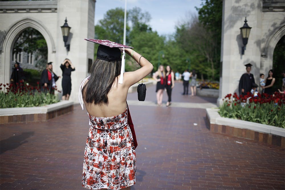 Kimia Mirzadeh takes pictures of her friends in front of the Sample Gates on Thursday.  Throughout the day, hundreds of graduates flocked to the corner of Indiana and Kirkwood to takes pictures in their caps and gowns.