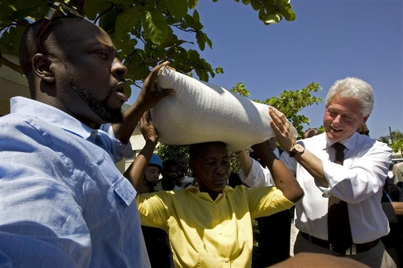 Haitian-American pop Singer Wyclef Jean, left, and former U.S. President Bill Clinton, right, aid a woman to raise a sack of rice which was donated by Jean's organization "Yele Haiti" in Cite Soleil in Port-au-Prince, Monday.  Clinton, Jean and UN Secretary General Ban Ki-moon, unseen, are trying to refocus international attention on Haiti in hopes of luring more aid to keep the impoverished country from sliding back into chaos. 