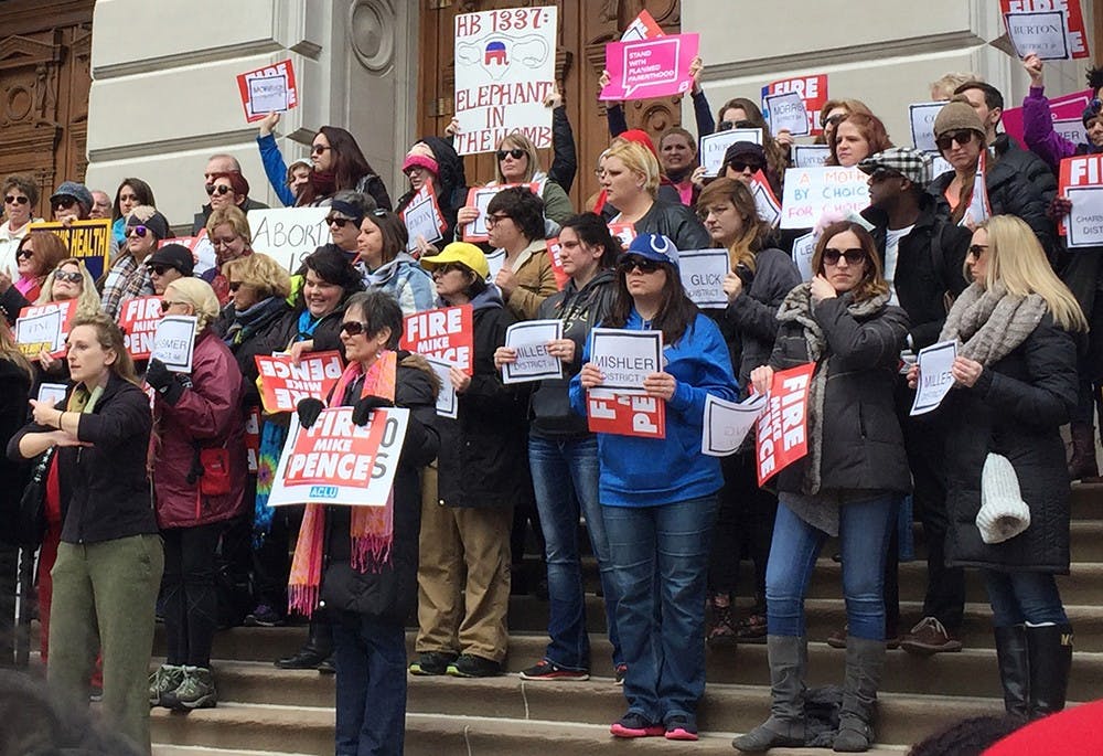 Rally attendees hold signs with the names of legislators who voted in favor of HEA 1337. Throughout the event, protesters chanted "Get them out" and "Fire Mike Pence."