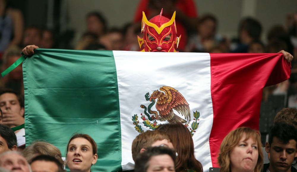 <p>A fan holds a Mexican flag wearing a red mask during the Opening Ceremonies of the 2012 Olympics at Olympic Stadium in London, England. </p>