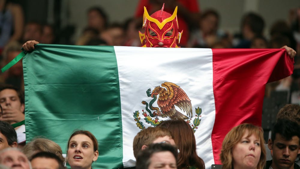 A fan holds a Mexican flag wearing a red mask during the Opening Ceremonies of the 2012 Olympics at Olympic Stadium in London, England. 