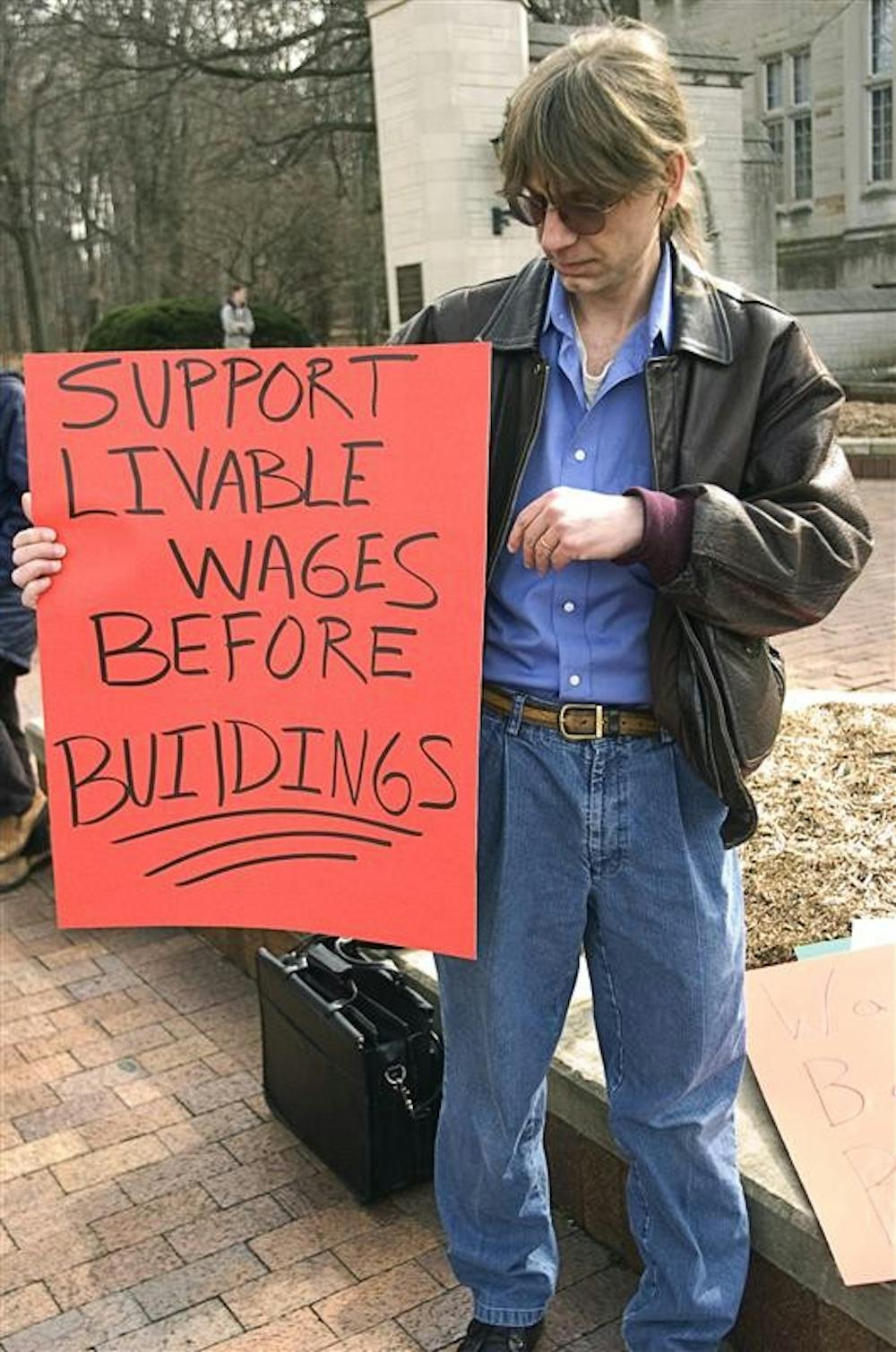 Peter Kaczmarczyk holds a sign Friday afternoon at the Sample Gates. Protesters gathered to speak out about the wages of IU and decisions to spend money on buildings.