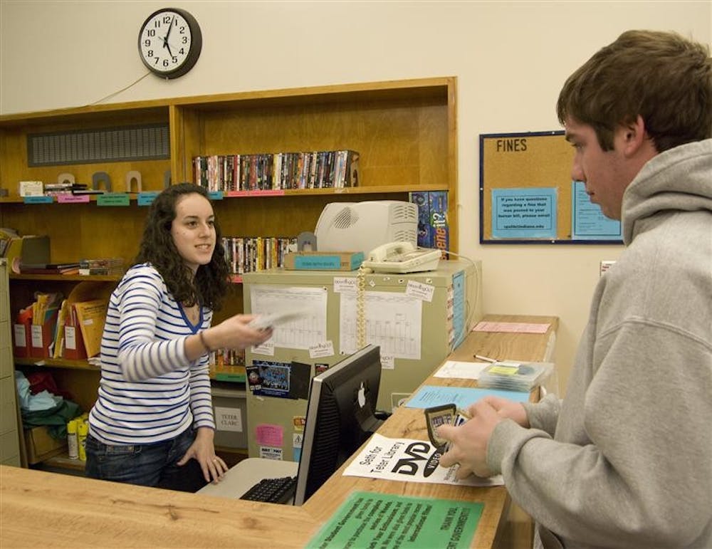 Sophomore Michelle Bloomfield checks out DVDs to freshman Adam Zacher Tuesday evening in the Teter Library. Students can be fined for not returning materials rented through the free service on time, which can result in penalties that unwittingly build up.