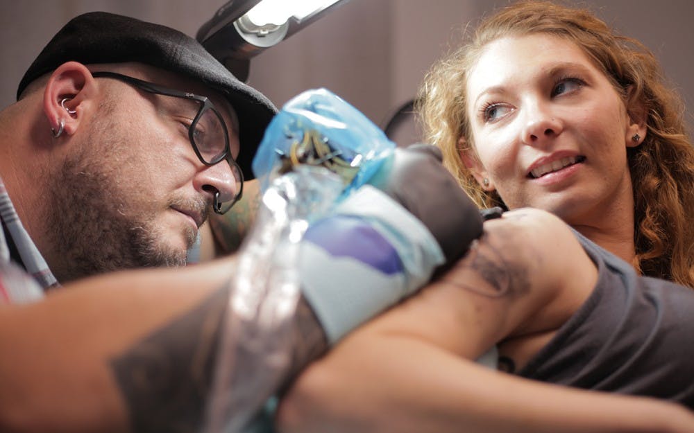 Artist Jon Rio inks Sarah Callon's arm with an electric guitar.  Callon drove from Brown County to have the work done at Rio's shop, Evil by the Needle.  