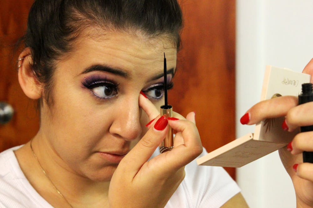 IU毕业生Vanesa Quiroga将液体眼线笔应用于她的假睫毛9月26日第15届年度嘉年华的后台。她的紫色眼影与她的quinceañeragown相匹配。 