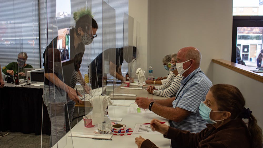 A voter submits their ballot to a poll worker behind plexiglass Oct 6. Lines have been long in Monroe County on most days since early voting began in Indiana on Oct. 6.
