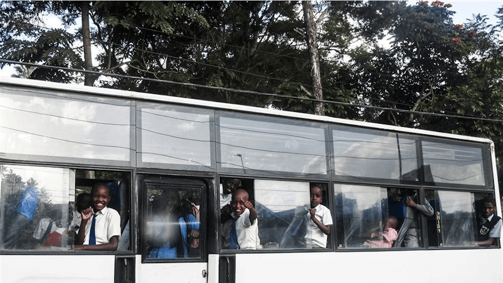 Students ride the bus and wave to pedestrians in Kenya.