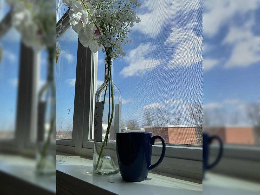 A mug and vase of flowers sit on a window sill. 
