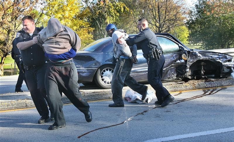 Indianapolis Metropolitan Police Department officers Scott Chandler, left, and Steven Renzulli, right, apprehend two bank robbery suspects from a car involved in a police pursuit that ended in a crash with another vehicle on Wednesday at E. 46th Street and Emerson Avenue.  Police say the driver who sped away from a bank robbery on the northeast side of Indianapolis was found dead inside the car after it crashed several miles away.  