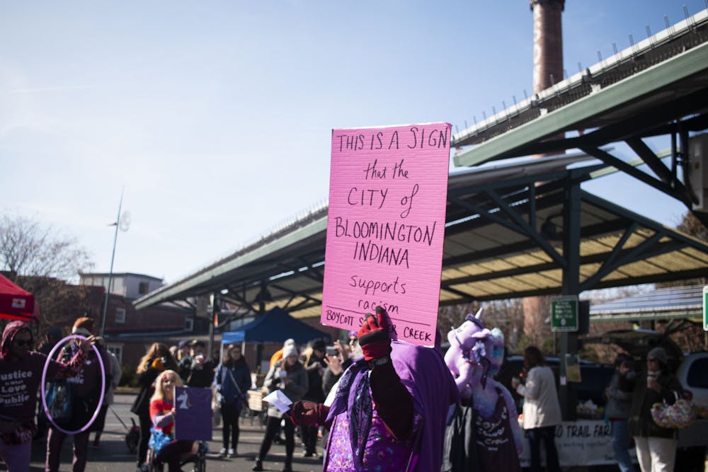 <p>Tom Westgard carries a sign Nov. 9 through the Bloomington Community Farmers’ Market in protest of Schooner Creek Farm, whose owners have been tied to a white nationalist group.  Five protesters cited at the Nov. 9 farmers market will not face charges.</p>