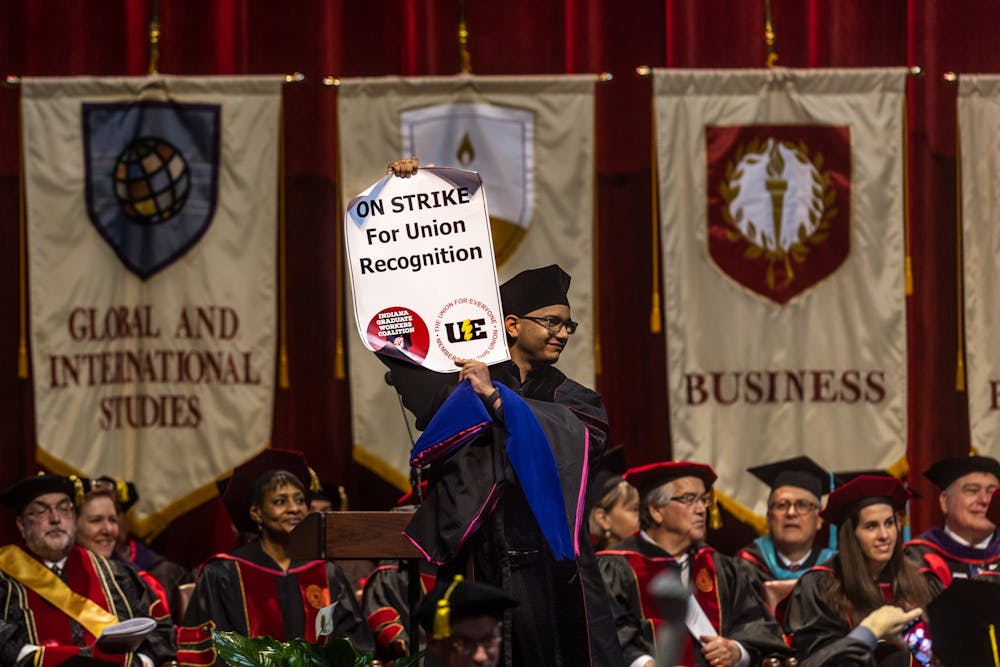 A graduating doctoral candidate holds up a sign for the Indiana Graduate Workers Coalition-United Electrical Workers strike while walking across stage May 6, 2022, in Simon Skjodt Assembly Hall. The IGWC-UE is striking to push the IU administration to recognize them as a union, according to the organization’s website. 