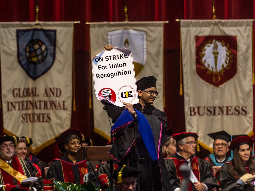 A graduating doctoral candidate holds up a sign for the Indiana Graduate Workers Coalition-United Electrical Workers strike while walking across stage May 6, 2022, in Simon Skjodt Assembly Hall. The IGWC-UE is striking to push the IU administration to recognize them as a union, according to the organization’s website. 