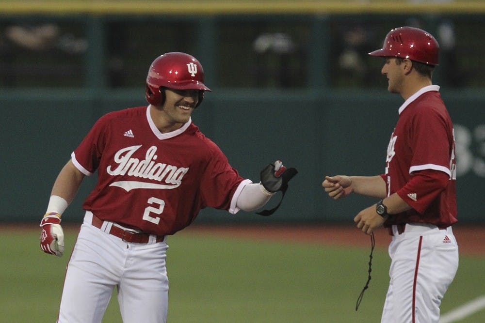 Junior outfielder Alex Krupa fist bumps assistant coach Matt Reida after making it to first base in the second game against Northwestern on Friday. The Hoosiers won the game 4-3.