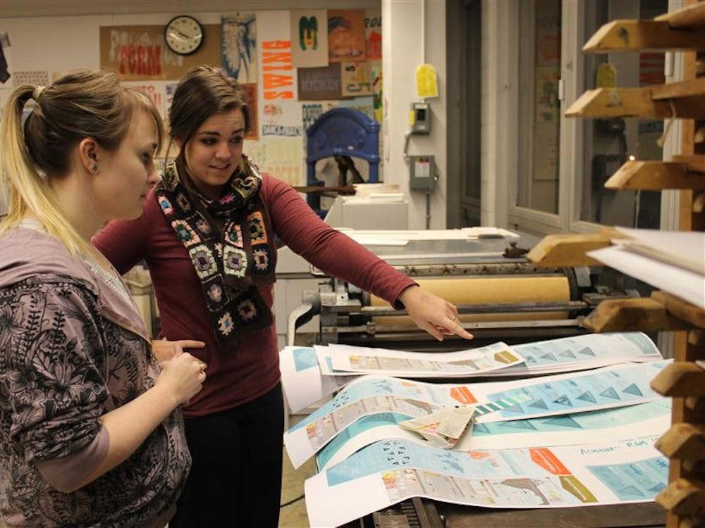 Senior Graphic Design BFA students Cristina Vanko (left) and Karen Radewald (right) compare the color on Radewald's preliminary mini prints. Her project "Watershed Moment" is nine feet tall.