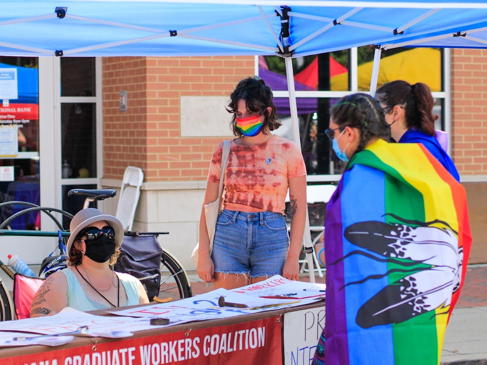 2021年8月28日，在布卢明顿市中心举行的布卢明顿骄傲活动上，Pridefest的参与者与印第安纳大学毕业生工人联盟的代表交谈。小贩和不同的组织在柯克伍德大道上设立了摊位。