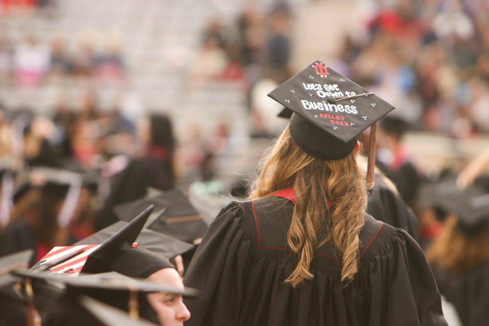 <p>A graduate with a cap reading “Let’s get down to business / Kelley 2022” searches the crowd for her guests May 7, 2022, in Memorial Stadium. Paying off student loan debt is often difficult for new graduates.</p>