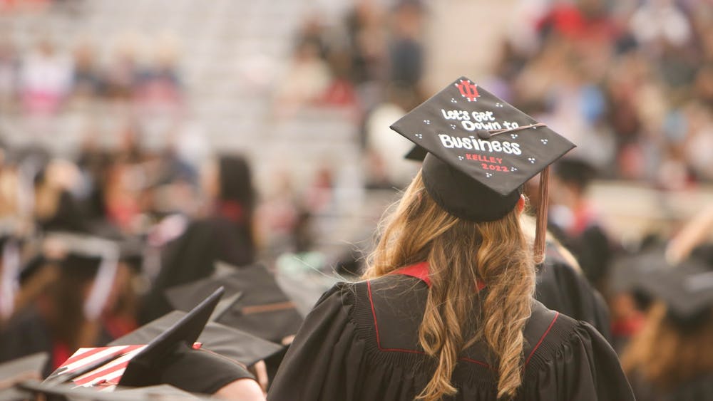 A graduate with a cap reading “Let’s get down to business / Kelley 2022” searches the crowd for her guests May 7, 2022, in Memorial Stadium. Paying off student loan debt is often difficult for new graduates.