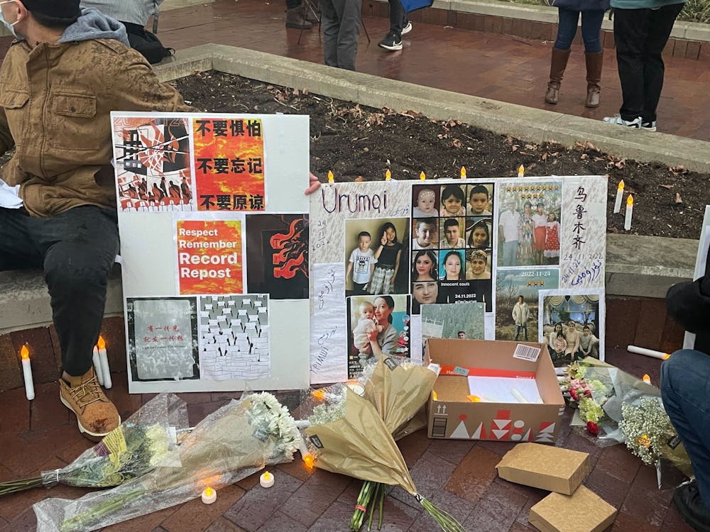<p>A demonstrator holds a sign depicting victims of fire and encouraging protests in China. Over 70 people gathered for a vigil honoring the victims of a fire in China and protesting the country’s zero COVID policy Friday at the Sample Gates.</p>